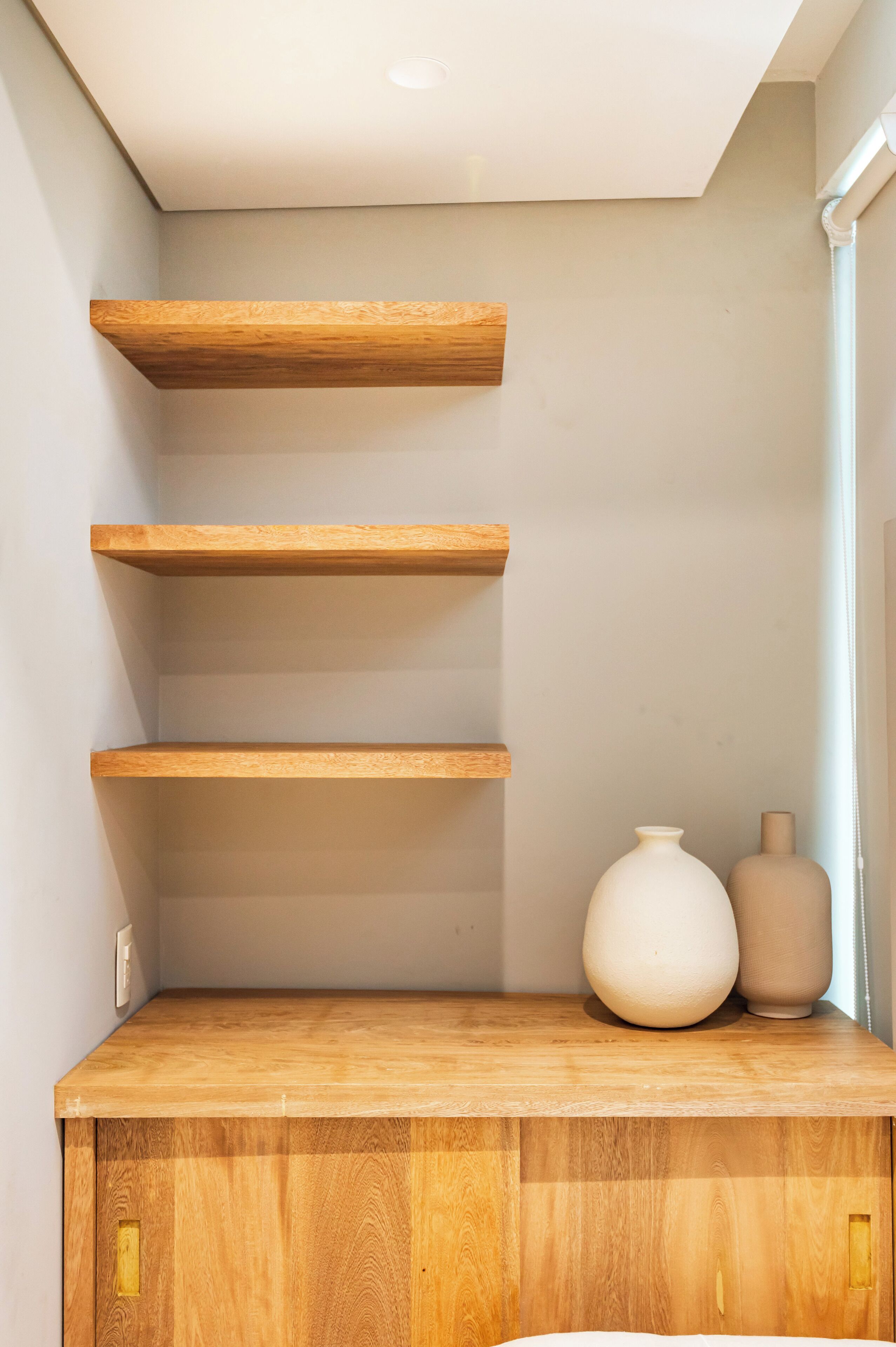 Una estantería de madera con tres repisas y un jarrón blanco en la repisa superior.
