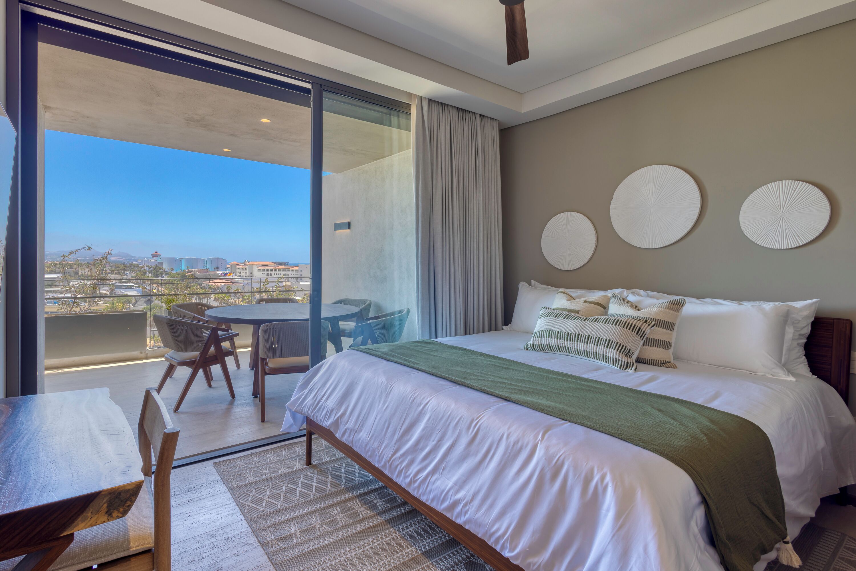 A modern hotel room with a large bed, a dining area, and a balcony with a city view.