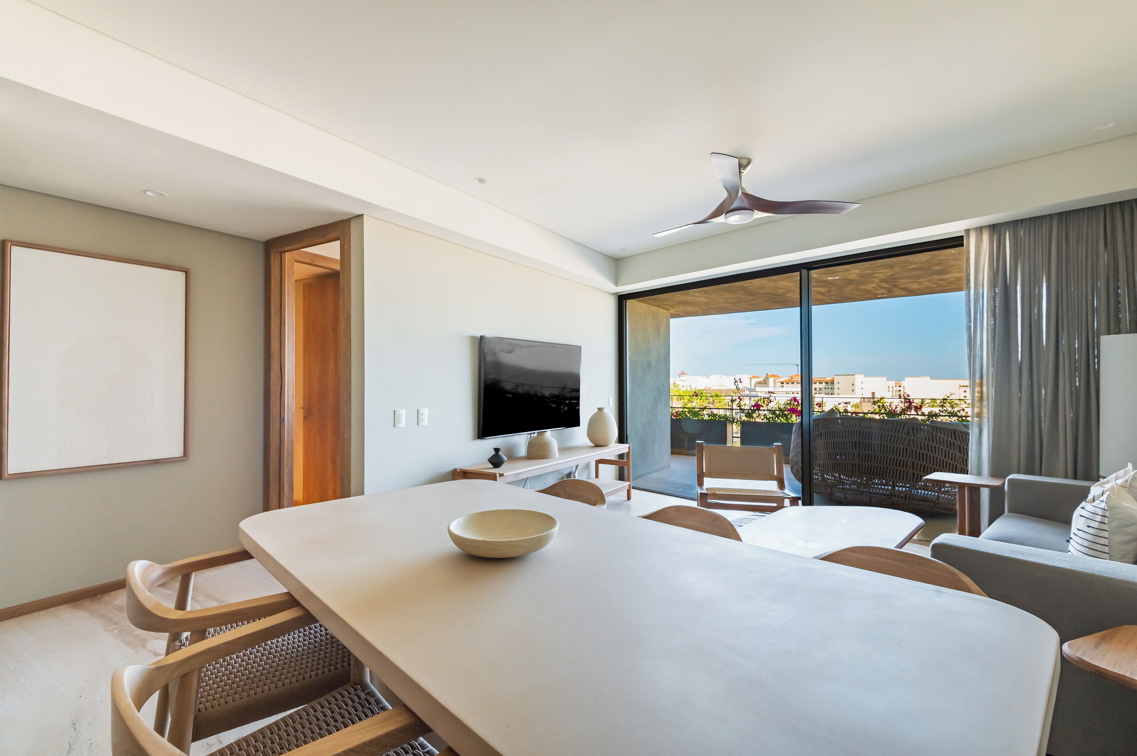 Habitación de hotel moderna con un amplio comedor, asientos cómodos, televisor de pantalla plana y un balcón con vista a la ciudad.