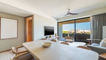 Habitación de hotel moderna con un amplio comedor, asientos cómodos, televisor de pantalla plana y un balcón con vista a la ciudad.