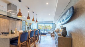 Une cuisine moderne dotée d’un îlot central, de chaises en bois, de luminaires suspendus et d’une grande fenêtre offrant une vue sur la verdure.