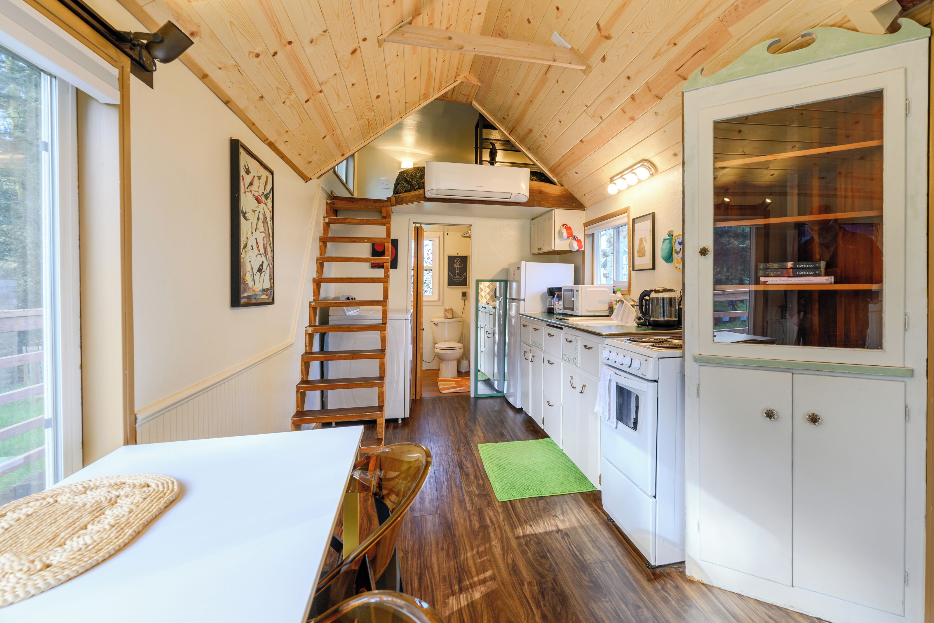 Cocina compacta con techo de madera, comedor con mesa y sillas, y vista al exterior a través de una ventana.