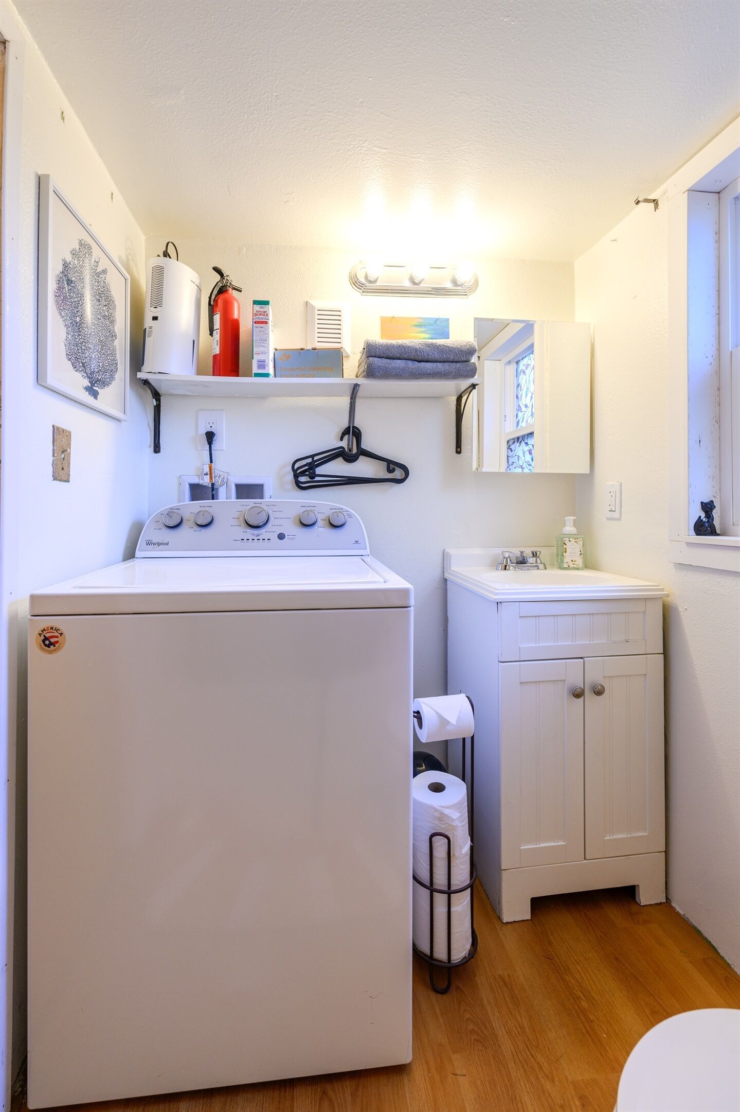 Une petite buanderie équipée d’un lave-linge et d’un sèche-linge à chargement frontal, d’un petit évier avec un miroir et d’un plancher en bois.