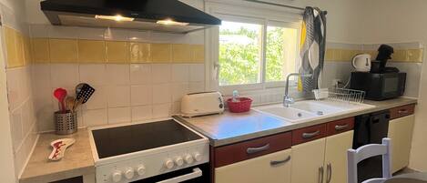 A compact kitchen with a stove, oven, and a microwave. There is a window with a view of greenery outside.