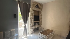 A living room with a stone fireplace, a television, a coffee table, and a sofa. - Gîte Lavande*Clim*Terrace*Community pool (Saint-Paul-Trois-Châteaux)