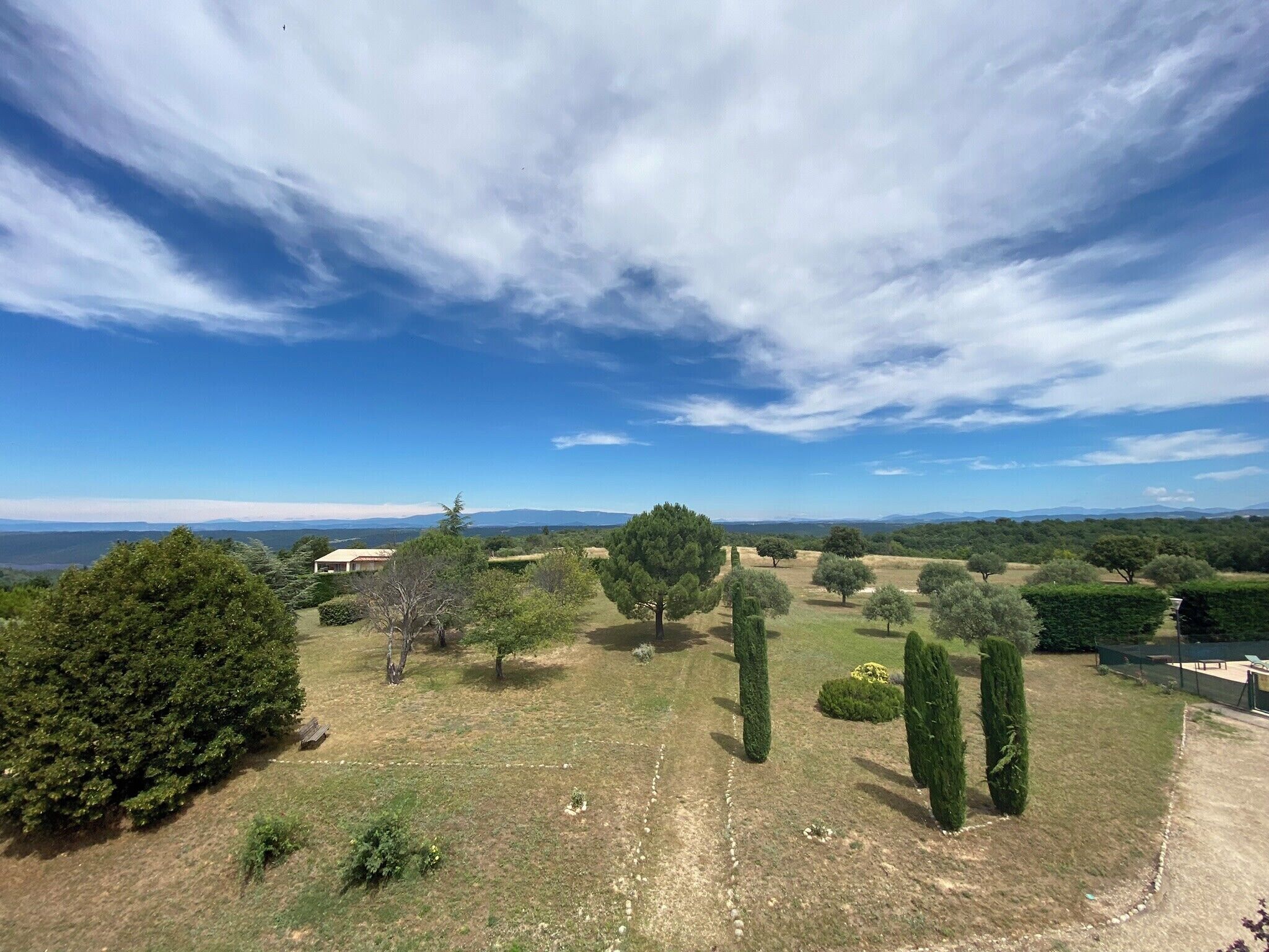 Paisatge rural amb cel serè, arbres i muntanyes llunyanes.