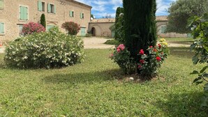 A stone building with a tiled roof, a well-maintained garden with various shrubs and flowers, and a tall, narrow tree. - 04B3: Beautiful T3 in the heart of lavender - pool (Brunet)