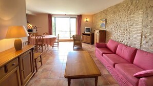 A living room with a sofa, a coffee table, a dining table with chairs, a television, and a kitchen area with a microwave. - 04B3: Beautiful T3 in the heart of lavender - pool (Brunet)