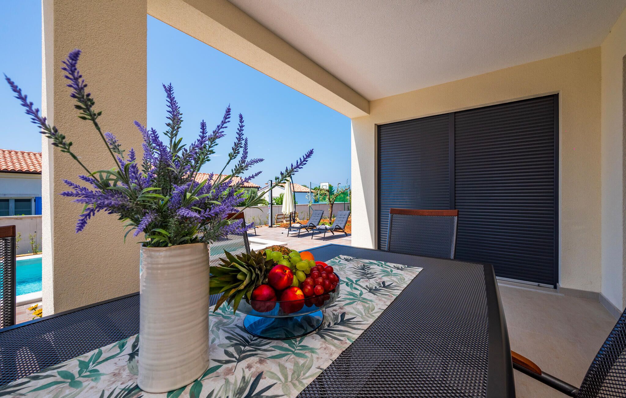 A balcony with a table, a vase with purple flowers, and a bowl of fruit.