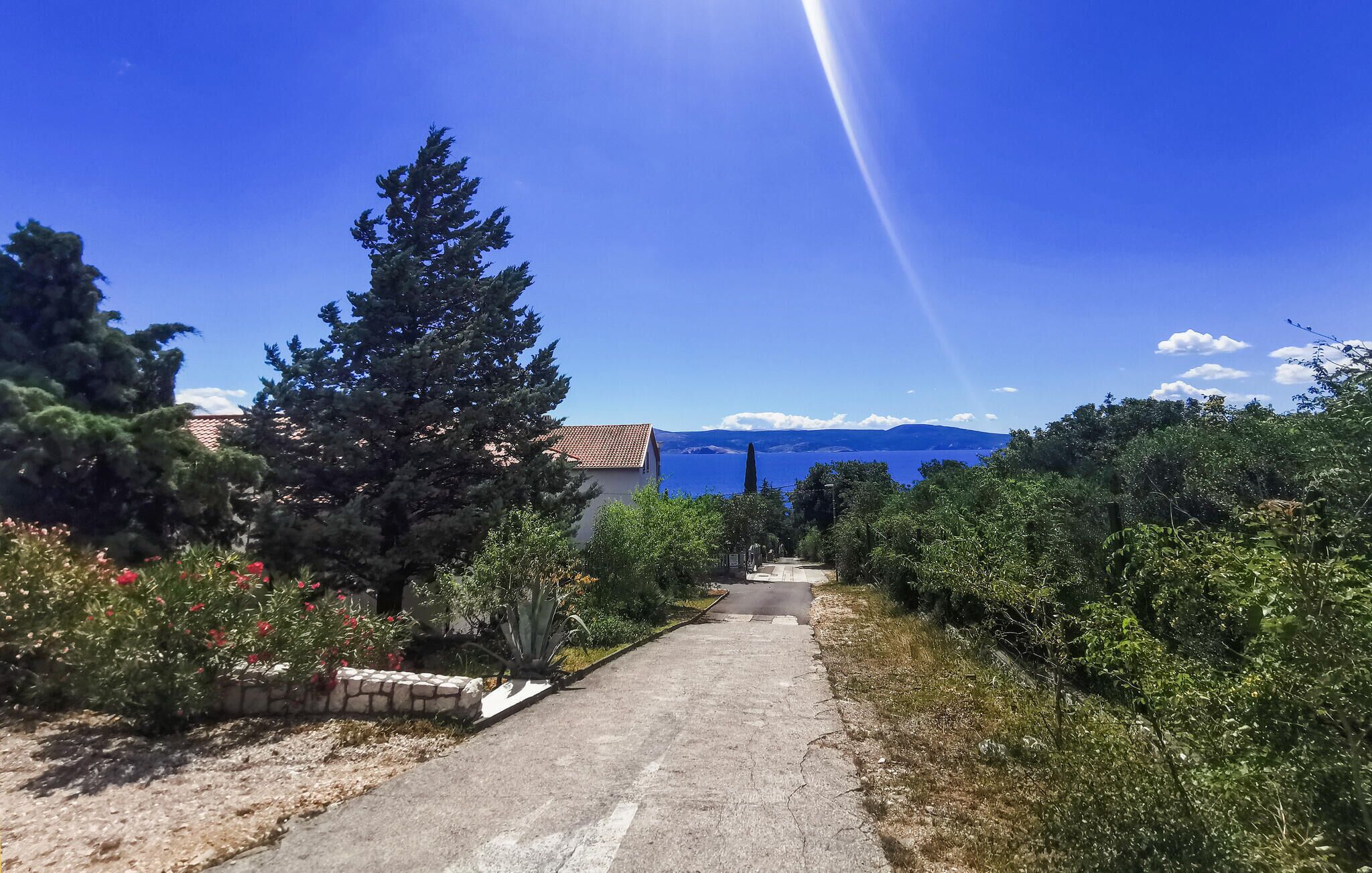 A paved pathway leading to a building with a view of the sea and mountains in the background.