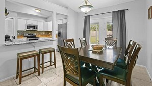 A modern kitchen with white cabinets, a central island, and a dining area with a wooden table and chairs. - BR Tropical Oasis in Port St Lucie (Port Saint Lucie)