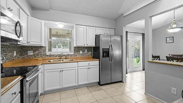 A modern kitchen with white cabinets, a stainless steel refrigerator, a built-in oven, and a granite countertop. - BR Tropical Oasis in Port St Lucie (Port Saint Lucie)