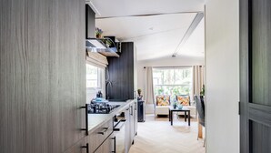 Een moderne keuken met een centraal eiland, een eethoek met een tafel en stoelen, en uitzicht op het groen door grote ramen.