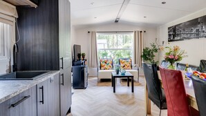 Een moderne keuken met een ingebouwde oven, een zithoek met een bank en een tafel, en een groot raam met gordijnen.