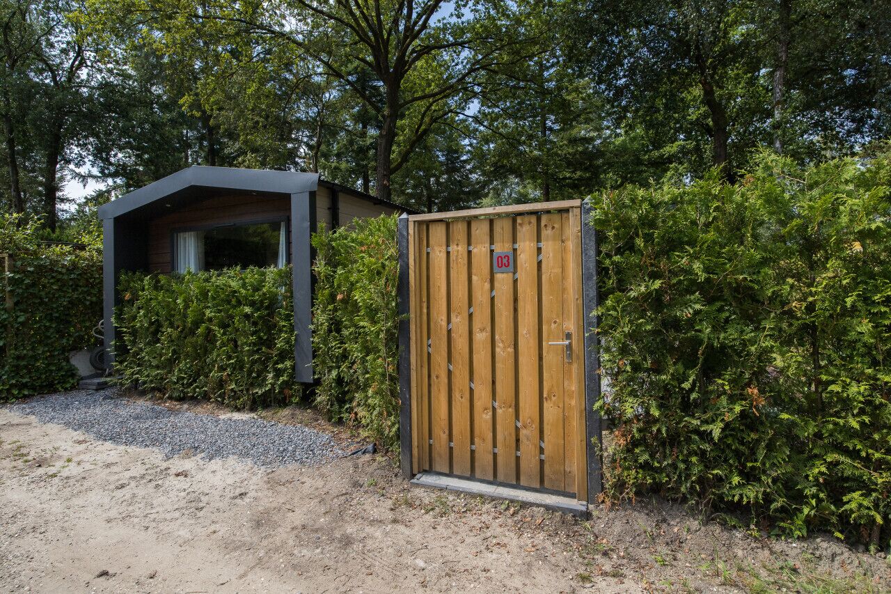 En träport med ett nummerplåt, en överbyggd konstruktion och tät vegetation.