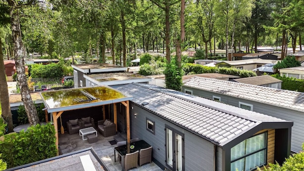 A modern house with a flat roof, a covered patio with outdoor furniture, and a view of the surrounding neighborhood.