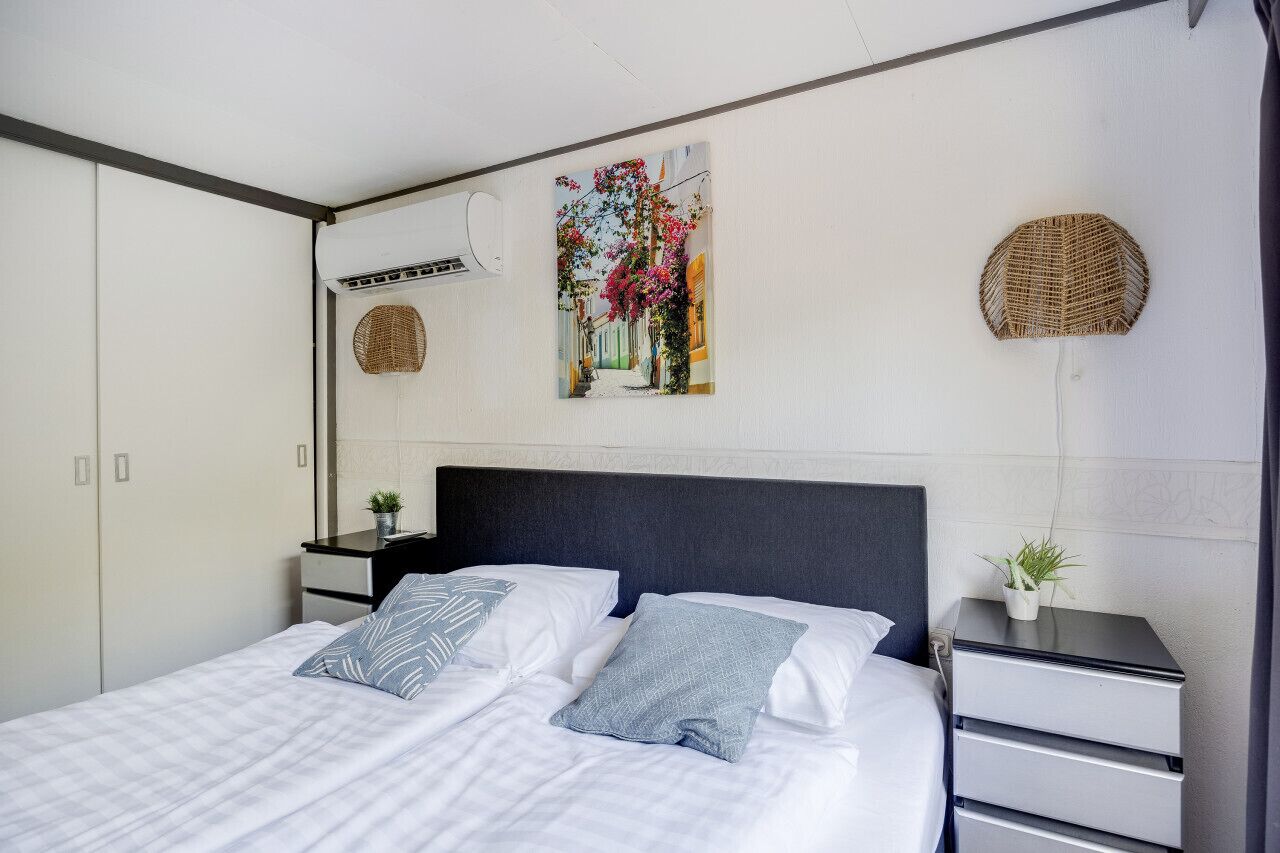 Une chambre bien rangée, avec un lit, deux tables de chevet et un climatiseur fixé au mur.