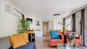 A modern living room with a sofa, a glass coffee table, and a red armchair. There is a kitchen in the background with white cabinets and a stove. - Stay With Private Hottub / Sauna (Voorthuizen)