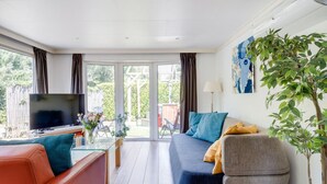 A modern living room with a sofa, armchair, TV, and a glass table. - Stay With Private Hottub / Sauna (Voorthuizen)