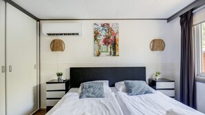 A double bed with white linens, two bedside tables with small potted plants, a dark headboard, and a wall-mounted air conditioner. - Stay With Private Hottub / Sauna (Voorthuizen)