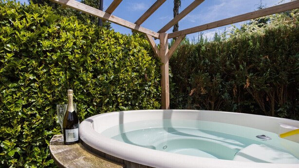 A hot tub in an outdoor setting with a wooden pergola overhead and lush greenery in the background. - Stay With Private Hottub / Sauna (Voorthuizen)