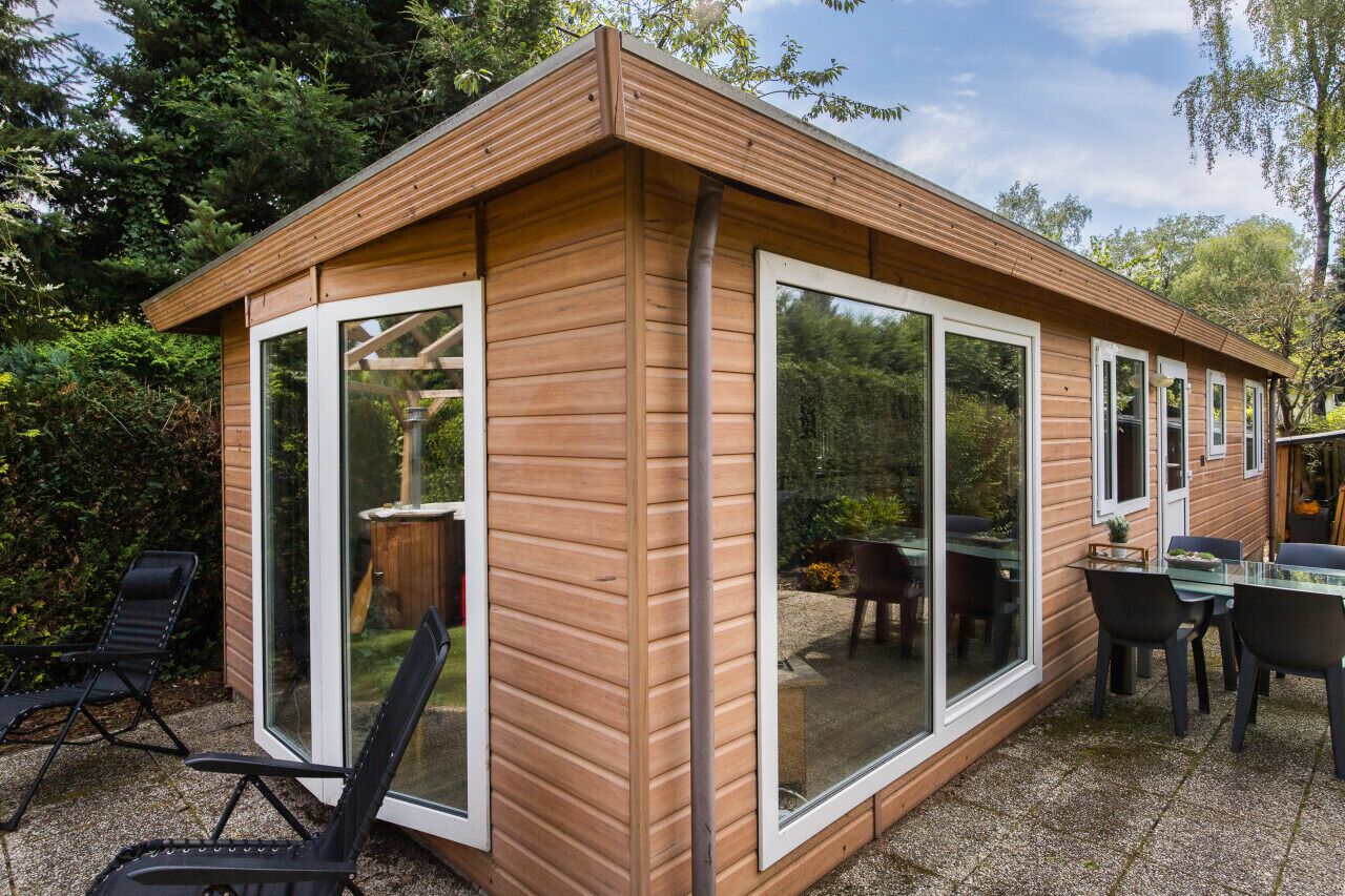 A wooden cabin with large sliding glass doors, a patio with chairs, and a table.