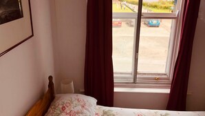 Un dormitorio con cama, una ventana con cortinas, un cuadro en la pared y vistas a un estacionamiento y zonas verdes.