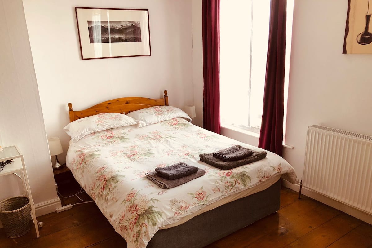 A neatly made bed with floral bedding, a wooden headboard, and two folded towels on the foot of the bed.