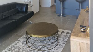A modern living room with a black leather sofa, a round coffee table, and a patterned rug. A dining area with a wooden table and bar stools is visible in the background. - Ponant-Archipel (Valras-Plage)