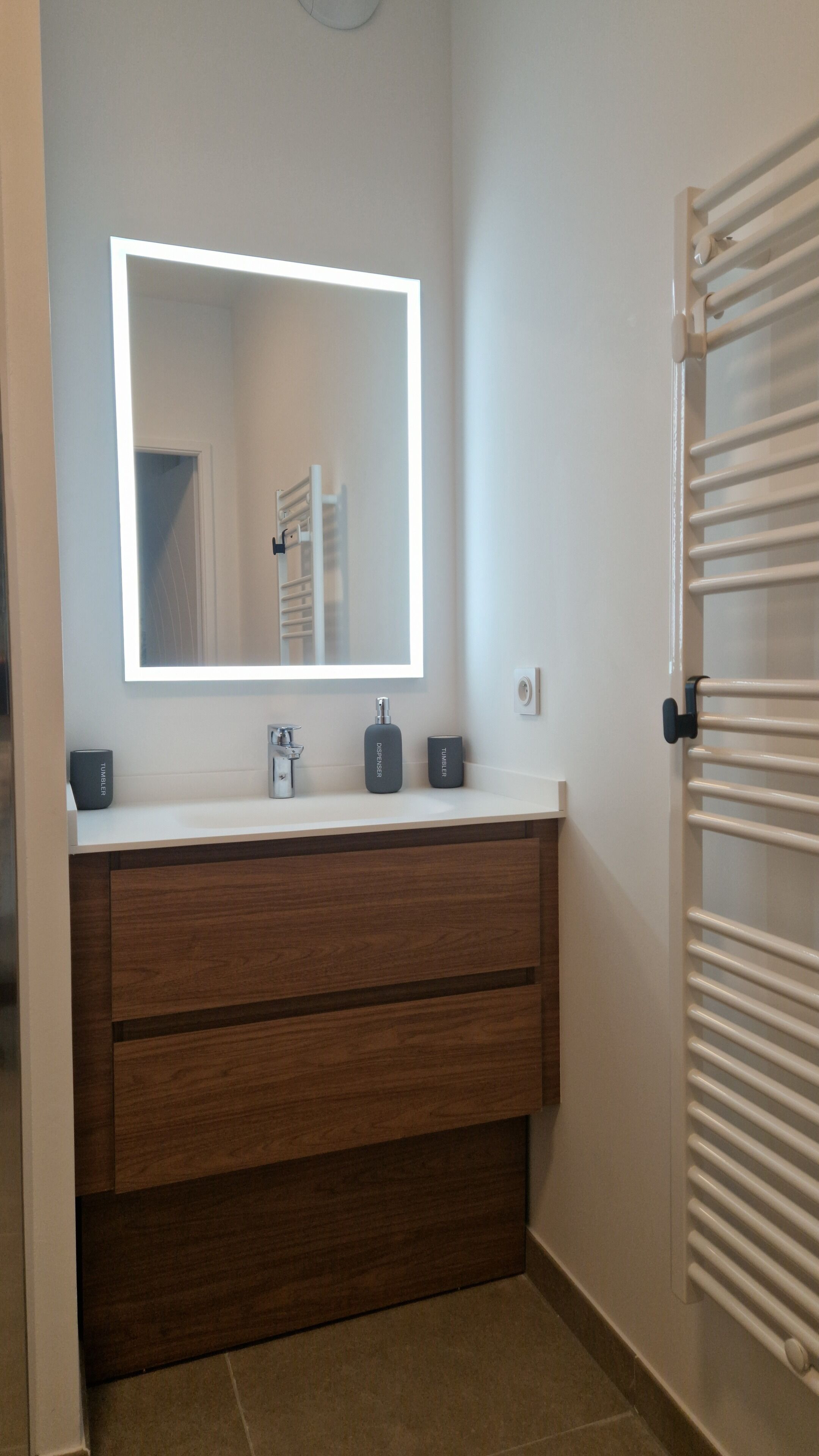 Un baño con tocador blanco, espejo con luz, toallero y radiador.