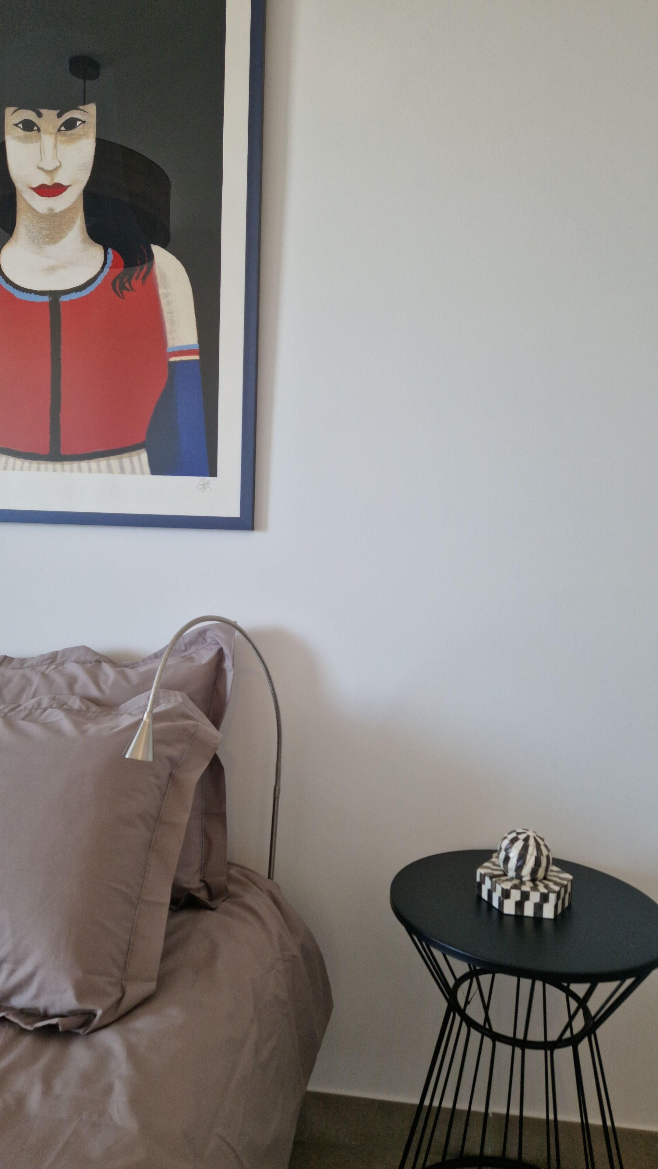 Una habitación con una cama, una mesita con un objeto decorativo y una obra de arte enmarcada en la pared.