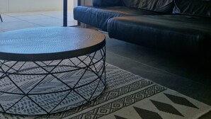 A modern living room with a black leather sofa, a round coffee table, and a patterned rug. There is a large window providing a view of the outdoors. - Ponant-Archipel (Valras-Plage)