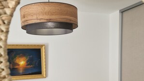 A bedroom with a bed, a bedside table with a lamp, a framed painting on the wall, and a hanging light fixture. - Archipelago Garden Side (Valras-Plage)