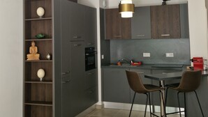 A modern kitchen with dark cabinetry, a dining area with two chairs, and a pendant light. - Archipelago Garden Side (Valras-Plage)