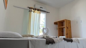 Un dormitorio con cama, mesita de noche, espejo, unidad de aire acondicionado, armario de madera y lámpara colgante.
