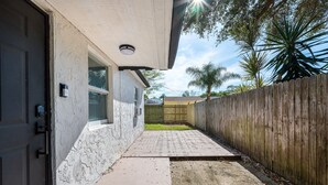 Un étroit sentier mène à une maison entourée d’une clôture en bois, dotée d’un chemin en béton et d’une porte équipée d’un dispositif de sécurité.