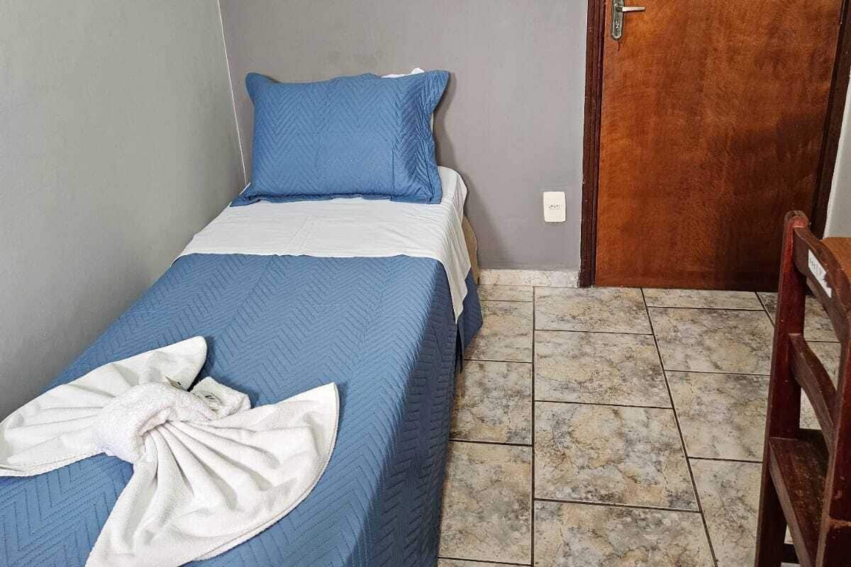 Una habitación pequeña con una cama individual, colcha azul, manta blanca y una puerta de madera.