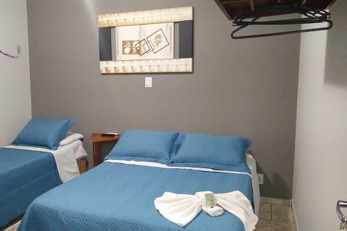 Habitación con dos camas, cada una con ropa de cama azul y almohadas blancas. Hay una pequeña mesa con un control remoto.