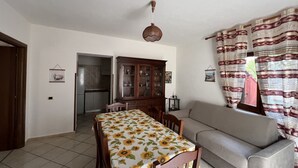 A dining area with a table covered in a sunflower tablecloth, a wooden cabinet, and a sofa.