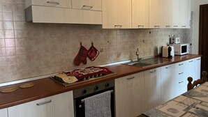 A kitchen with light wooden cabinets, a stainless steel sink, a microwave, and a stove.
