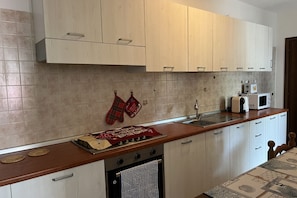A kitchen with light wooden cabinets, a stainless steel sink, a microwave, and a stove.