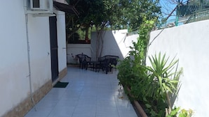 A patio area with a tiled floor, a black metal table and chairs, and a potted plant.
