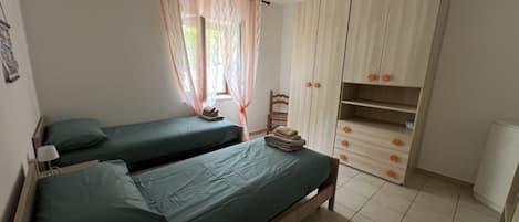A bedroom with two single beds, a wardrobe, and a window with curtains.