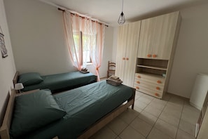 A bedroom with two single beds, a wardrobe, and a window with curtains.