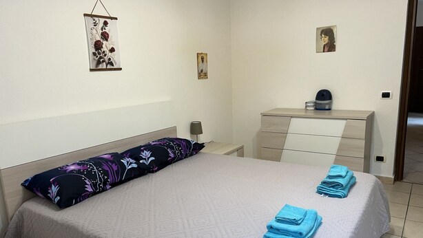 A neatly arranged bedroom with a bed, pillows, a bedside table, a dresser, and wall art.
