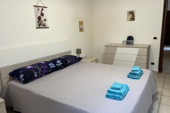 A neatly arranged bedroom with a bed, pillows, a bedside table, a dresser, and wall art.