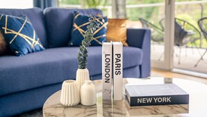 En moderne stue med en blå sofa, et sofabord med dekorative vaser og bøger med titlerne 'LONDON' og 'NEW YORK'.