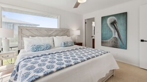 A bedroom with a bed, a ceiling fan, a window, and a painting of a pelican on the wall. - Pet friendly house across from the ocean, 30 day minimum stay (Fernandina Beach)