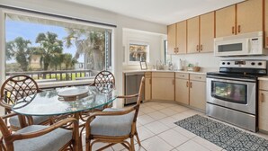 A modern kitchen with a glass dining table, wicker chairs, a stainless steel oven, and wooden cabinets. - Pet friendly house across from the ocean, 30 day minimum stay (Fernandina Beach)