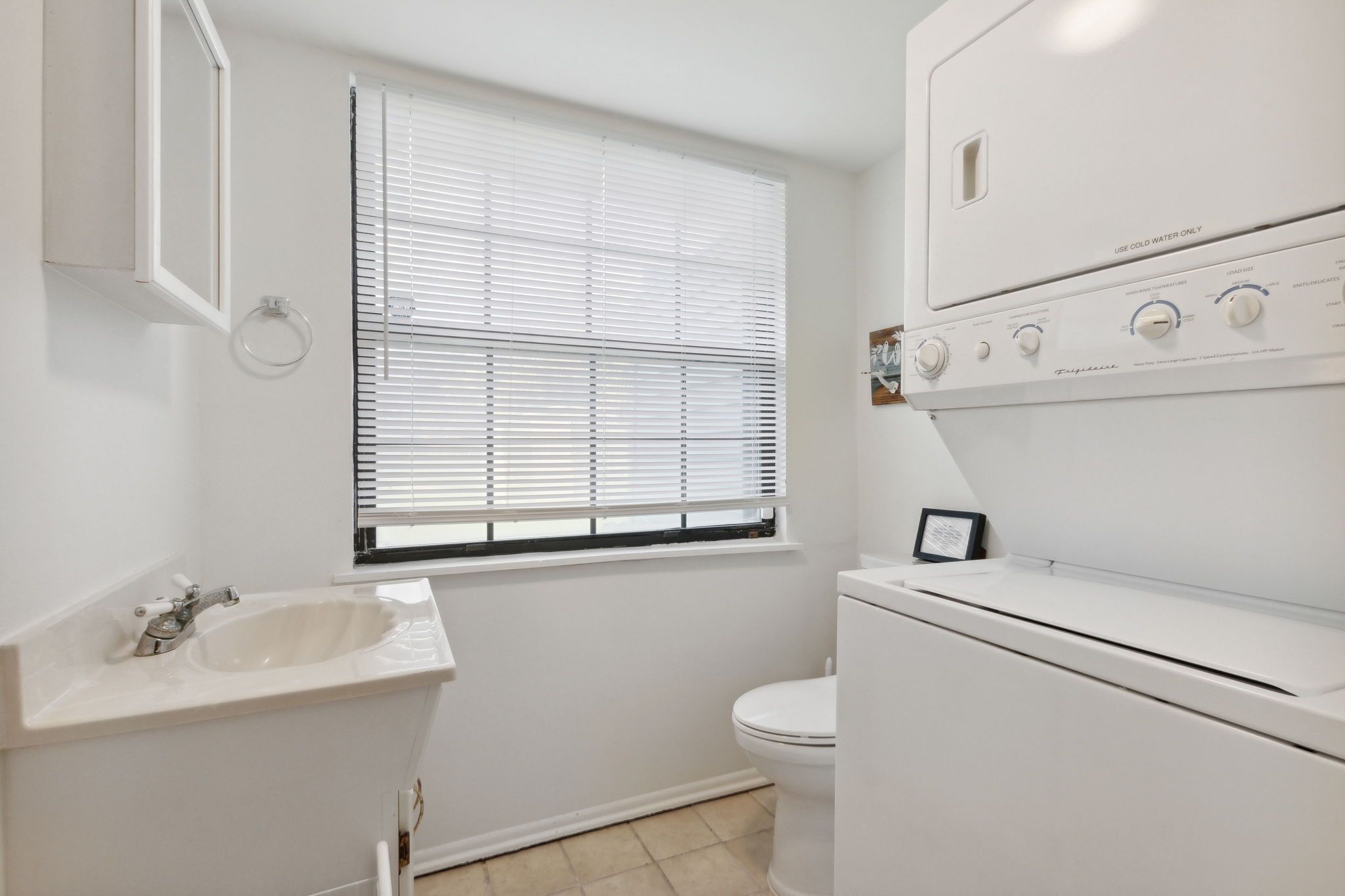 A bathroom with a sink, toilet, and a stacked washer and dryer.